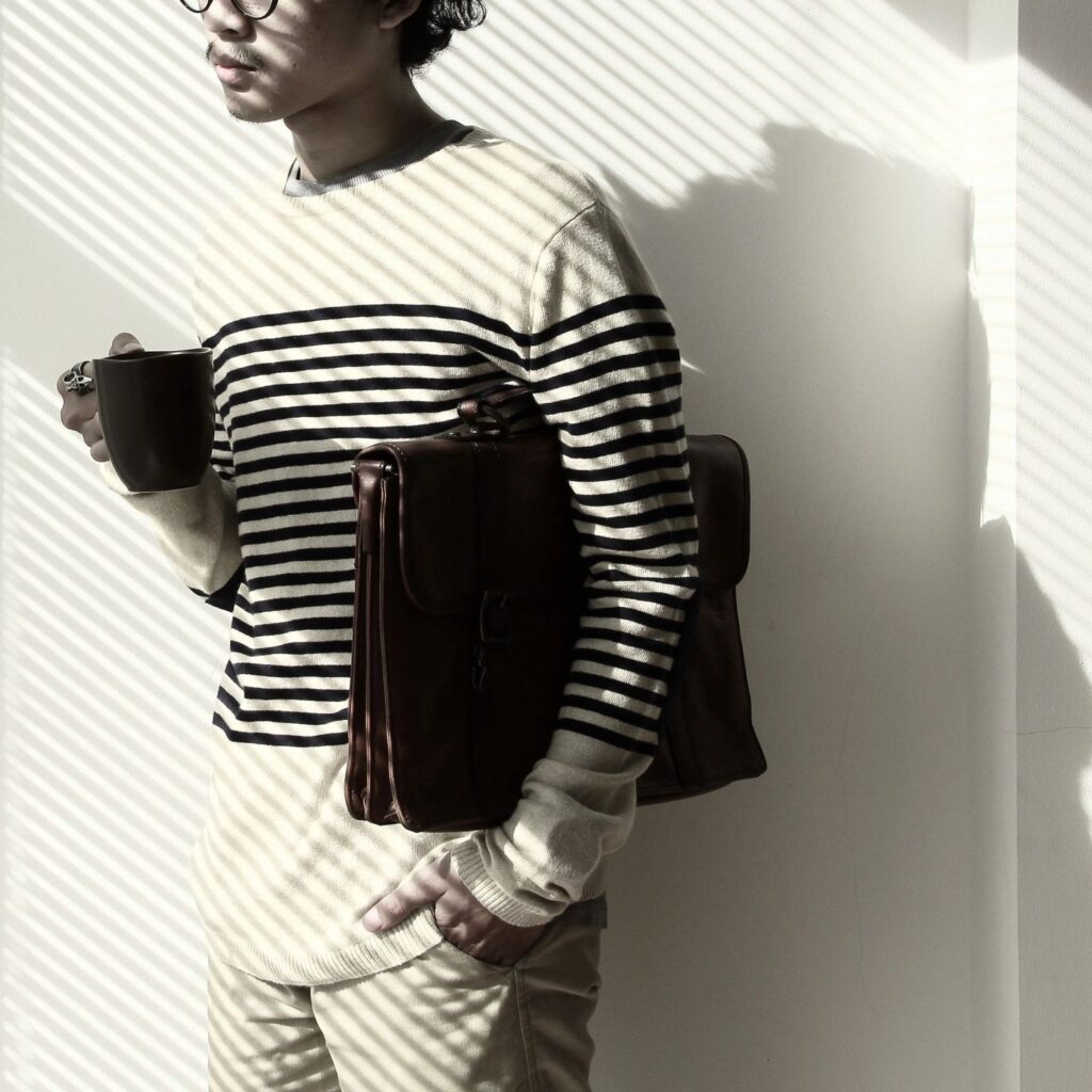 man with white shirt with black stripes holding a cup and holding a brief case in the other arm